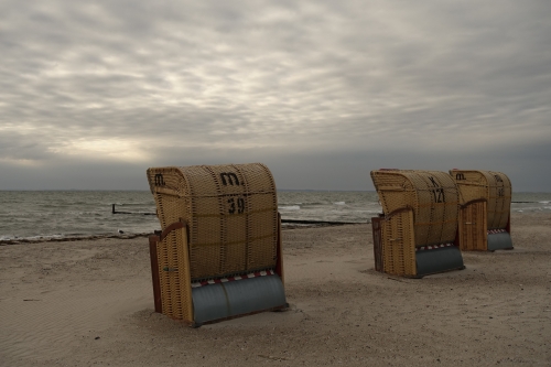 Drei verlassene Strandkörbe auf einsamem Sandstrand unter grauen Wolken
