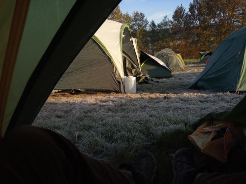 Blick aus einer Zeltöffnung auf viele Zelte und eine gefrorene Wiese in der Morgensonne