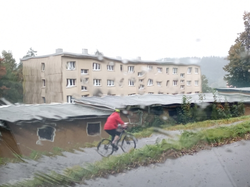 Verschwommener Mountainbiker vor DDR-Plattenbau, durch eine regennasse Scheibe betrachtet
